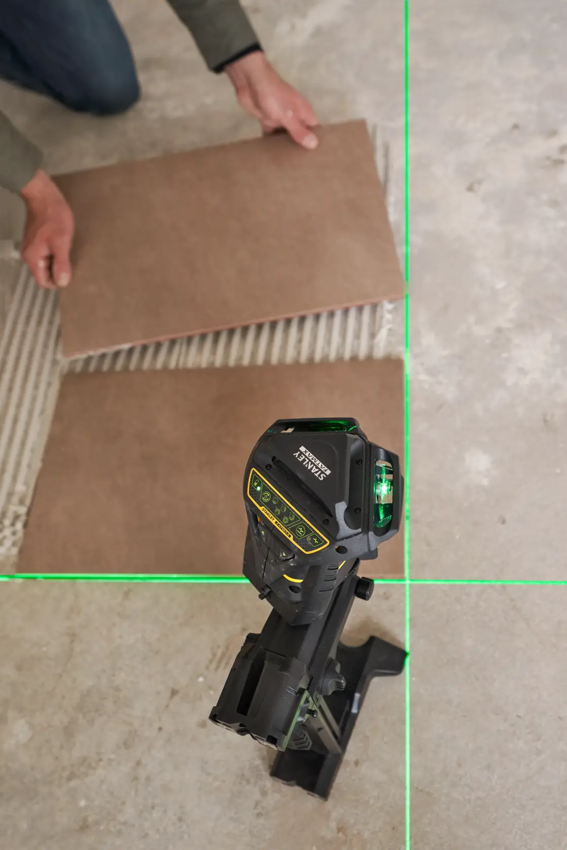 STANLEY FMHT1-77356 laser level on stand projecting green lines for tile alignment, photography view from above.