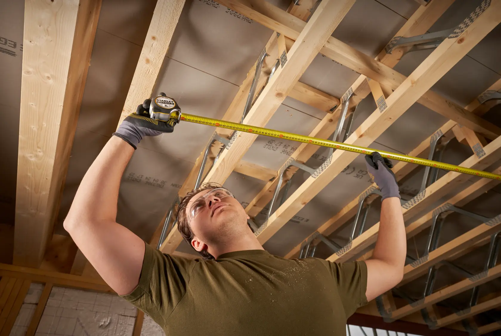 STANLEY FMHT38214-0 Maßband misst Holzbalken an einer Decke in einem Innenausbau.