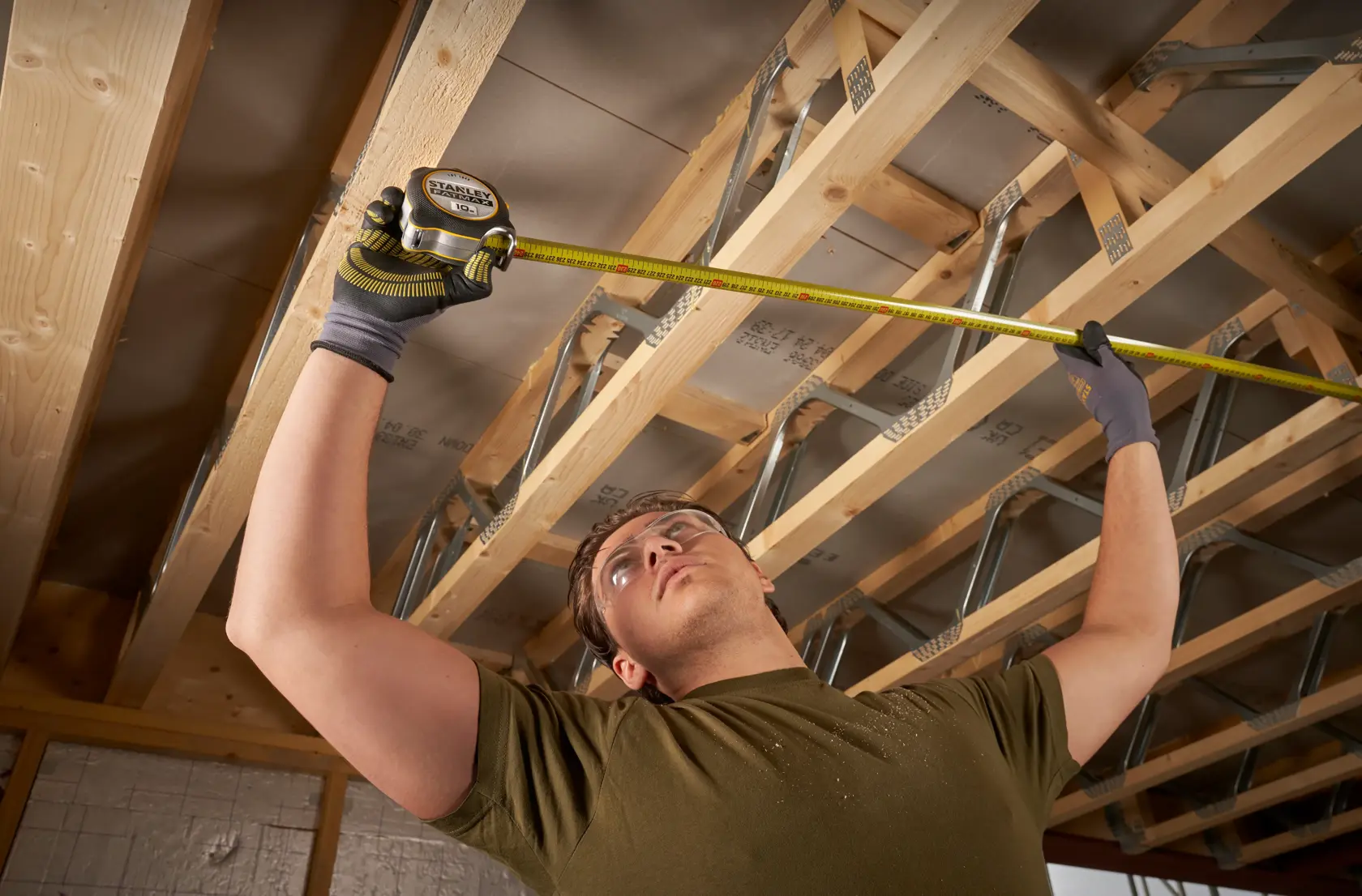Photo of a worker measuring ceiling joists with a STANLEY FMHT38232-0 tape measure in a construction area.