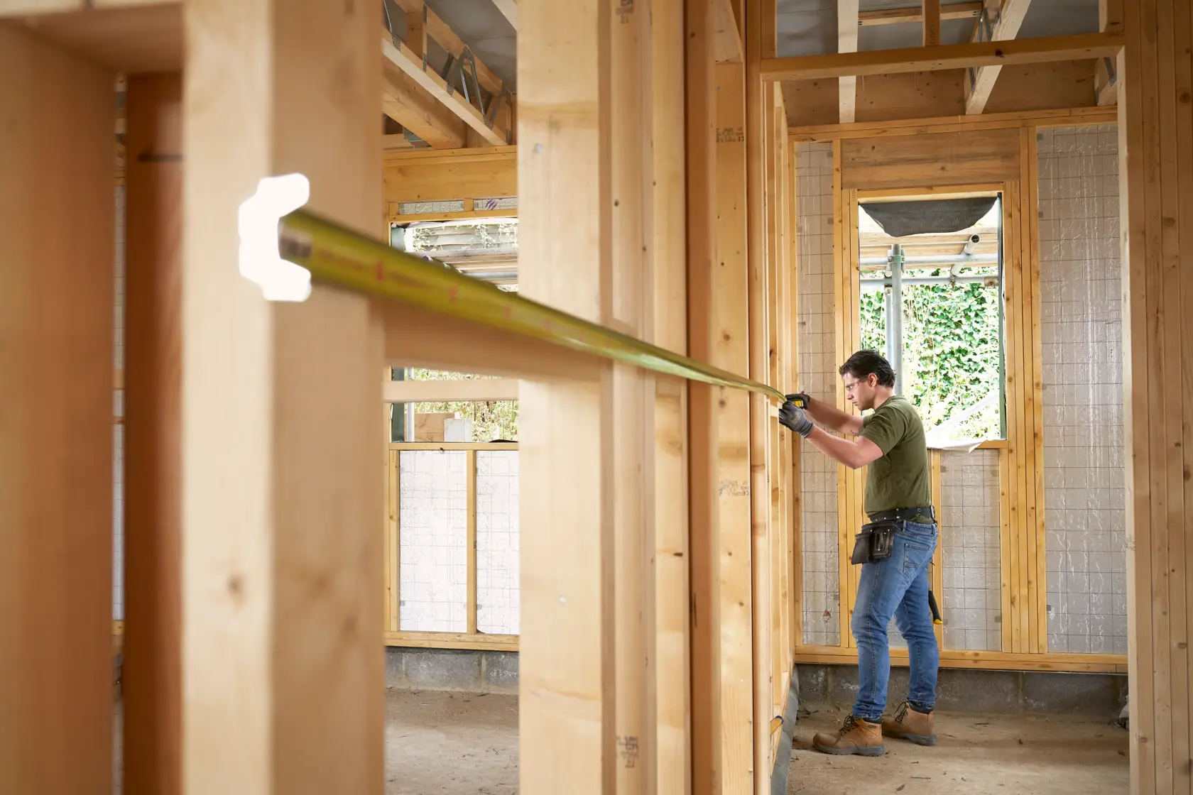 STANLEY FMHT38232-0 tape measure extended by worker inside wooden house frame, side view, construction site.