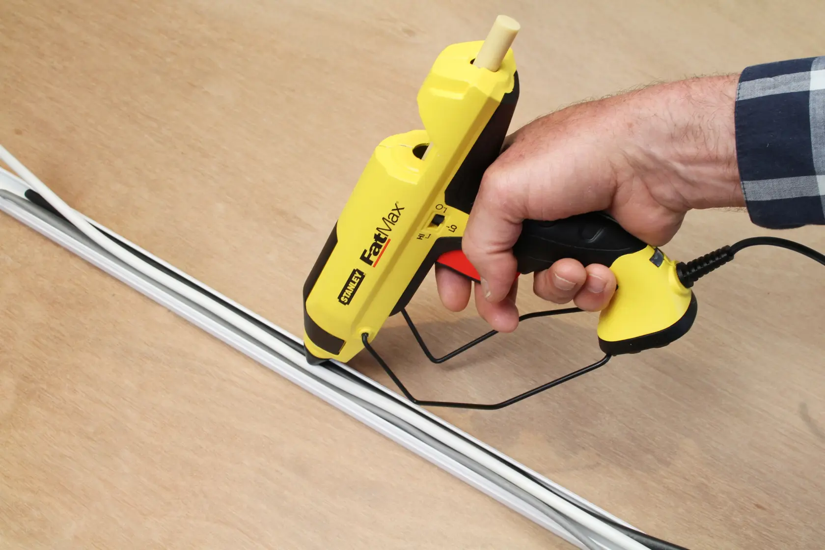 STANLEY FMHT6-70418 yellow glue gun in use applying adhesive to white trim on wood surface.