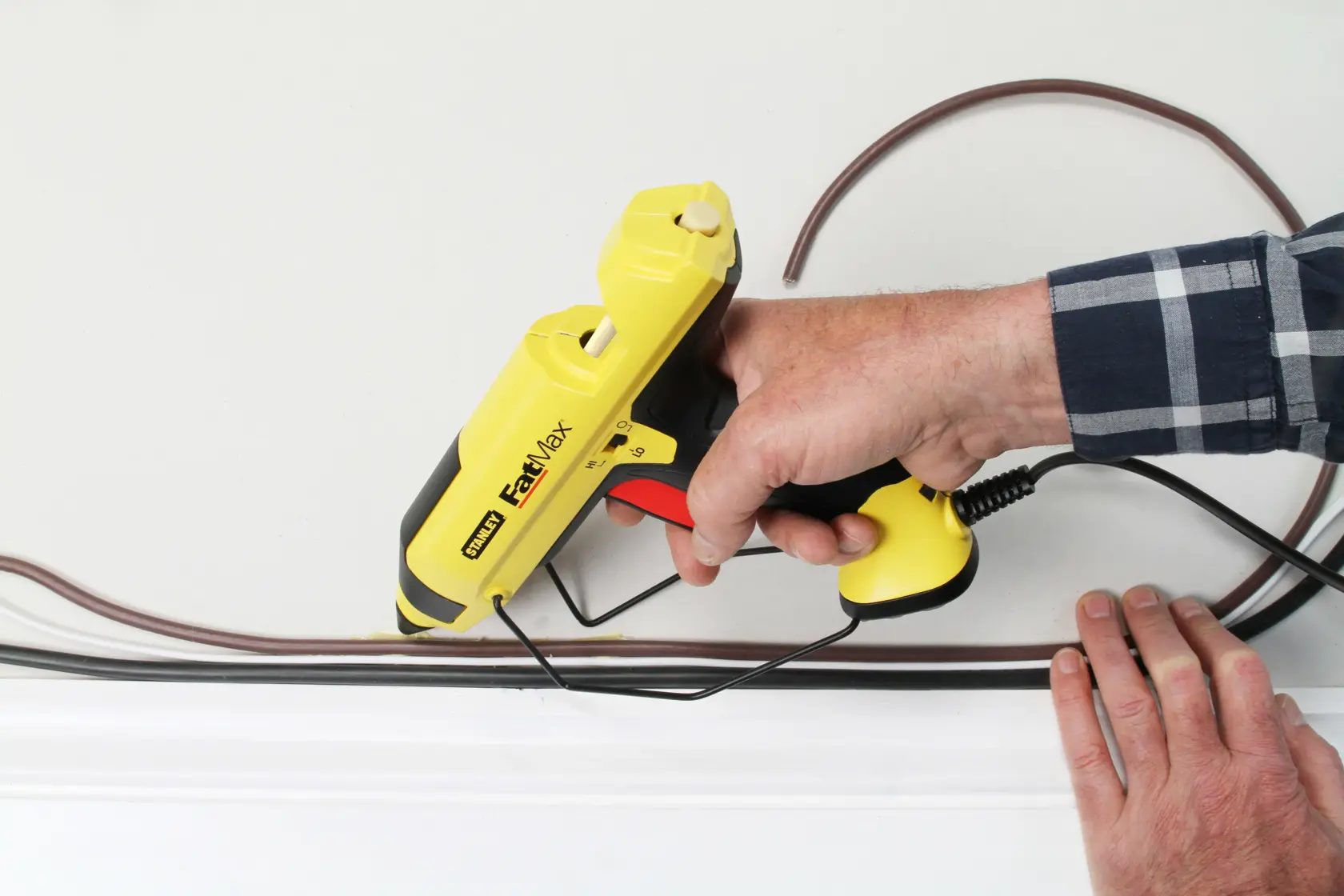 STANLEY FMHT6-70418 yellow FastMax glue gun in use for cable installation on a wall.