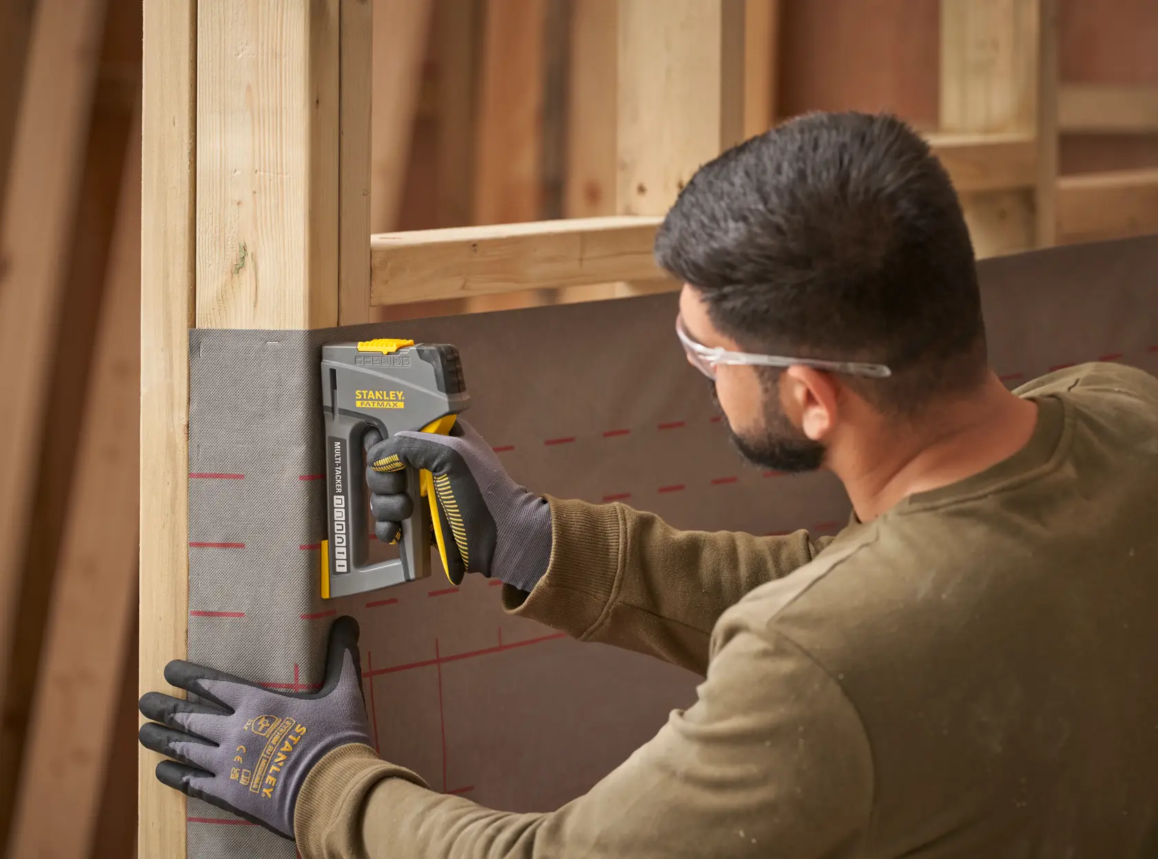 STANLEY FMHT6-70868 heavy-duty stapler used to fasten material to wooden frame, side view, person wearing gloves.