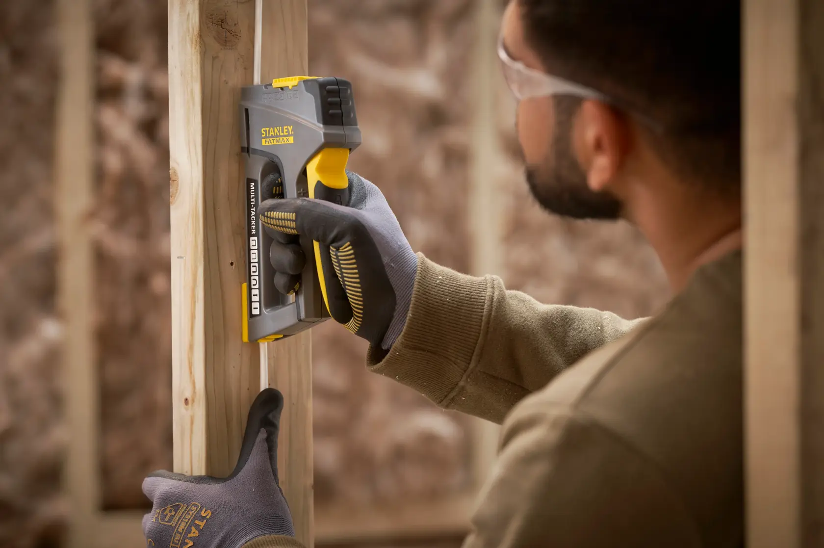 STANLEY FMHT6-70868 staple gun in use on wooden frame, close-up photography of tool and gloved hand.