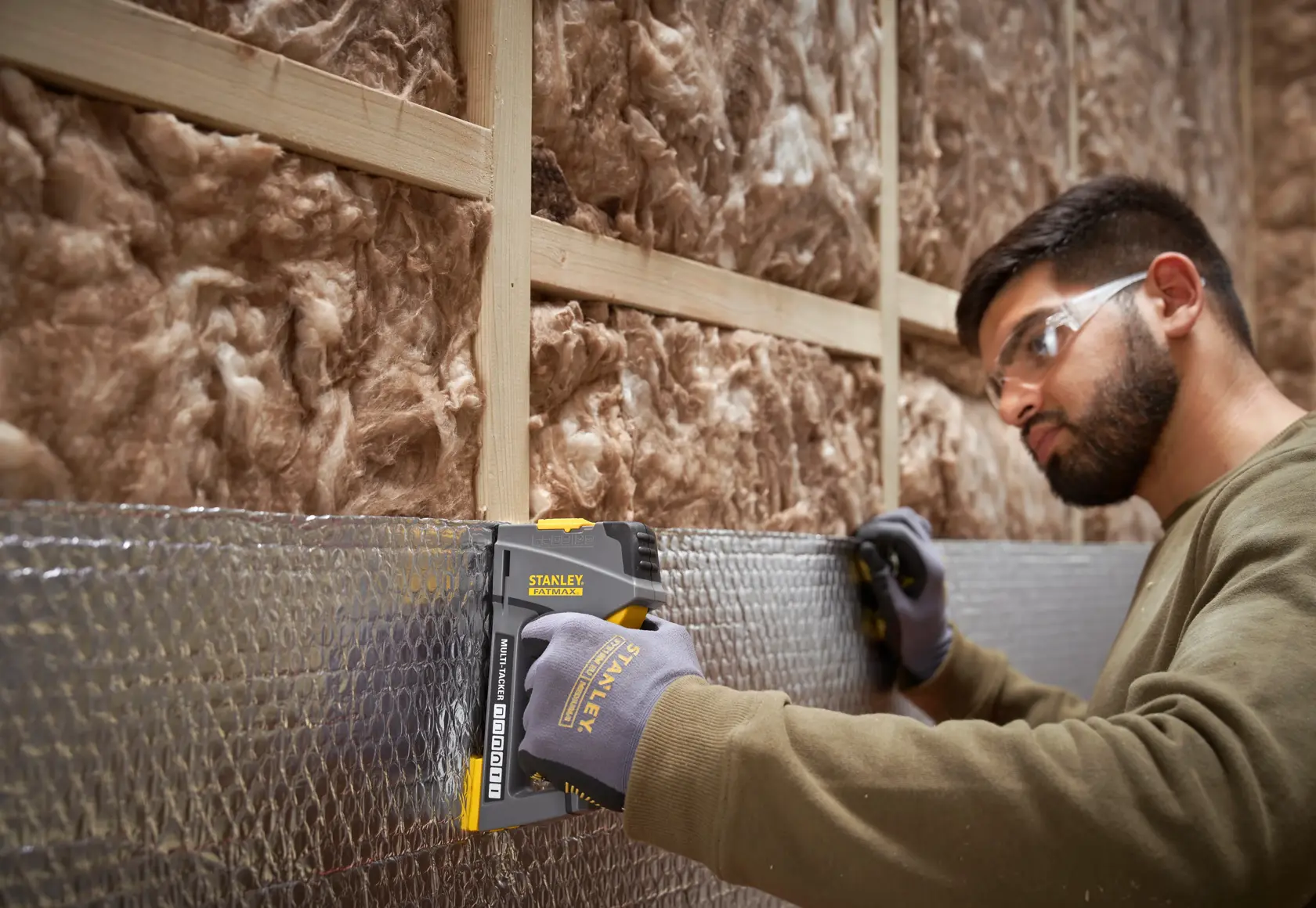 STANLEY FMHT6-70868 staple gun used on insulation by gloved worker, shown in construction setting.