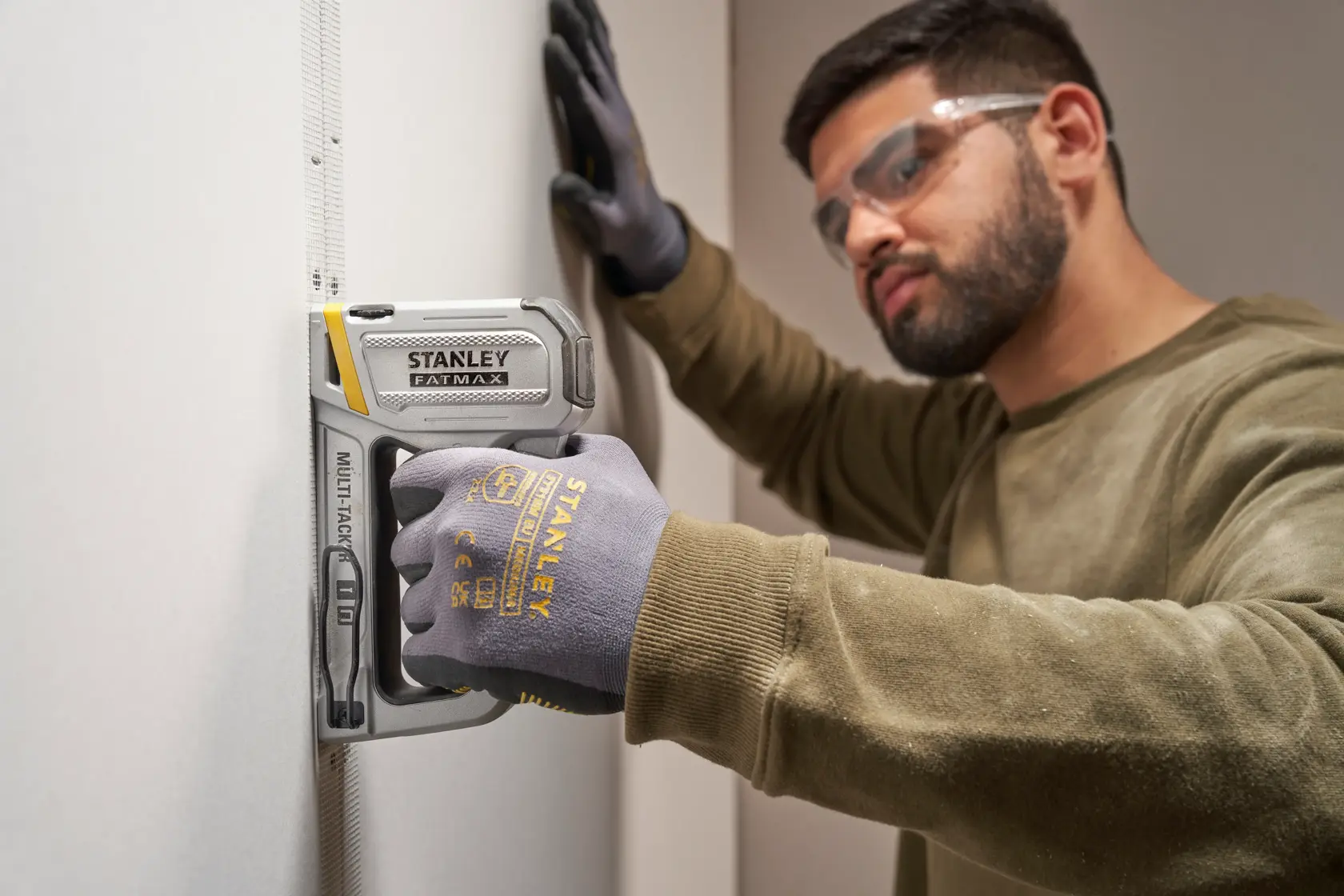 Photo of a person using a STANLEY FMHT70250-0 staple gun on drywall, wearing STANLEY gloves.