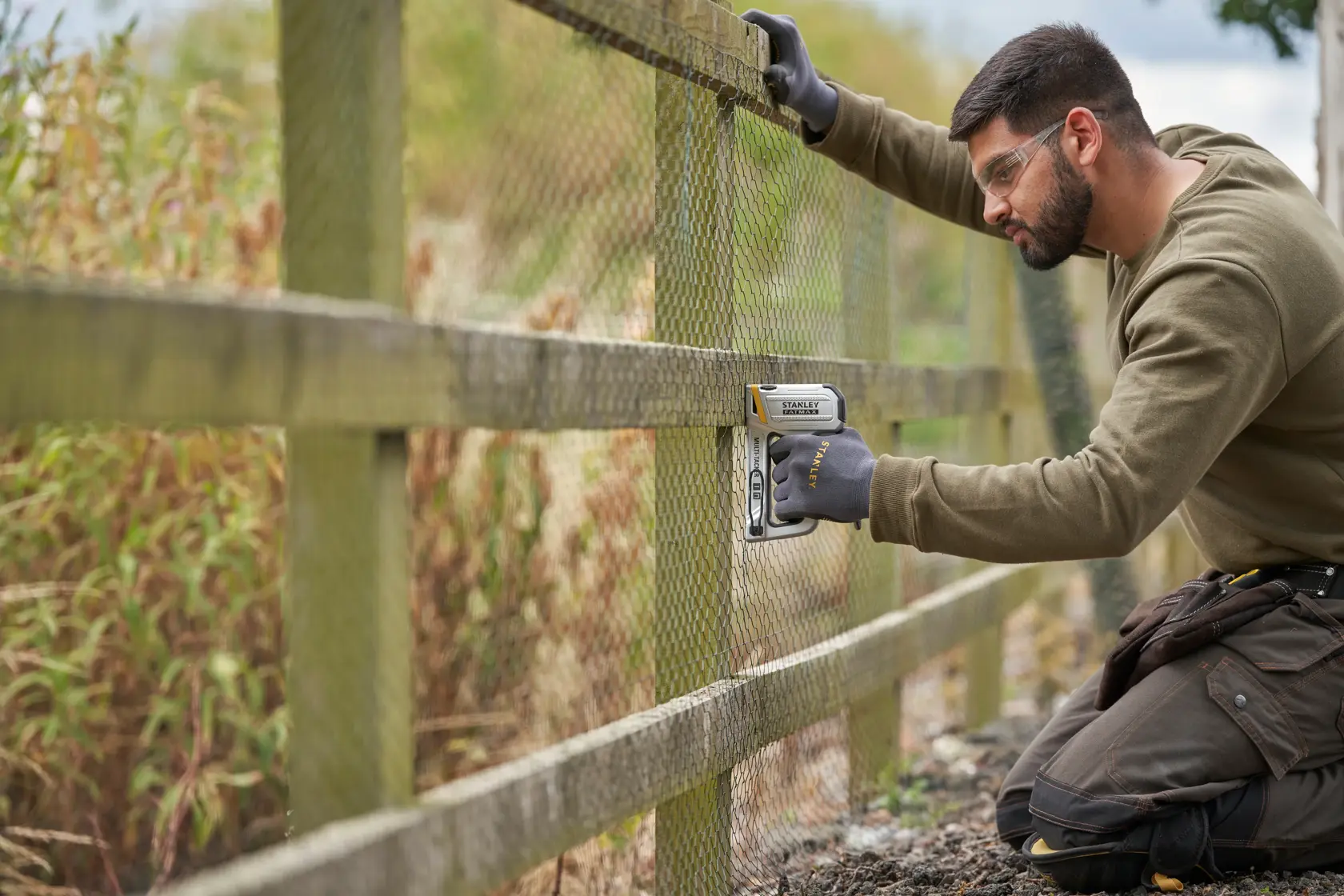 Photo of STANLEY FMHT70250-0 heavy duty stapler used to secure mesh to a wooden fence outdoors.