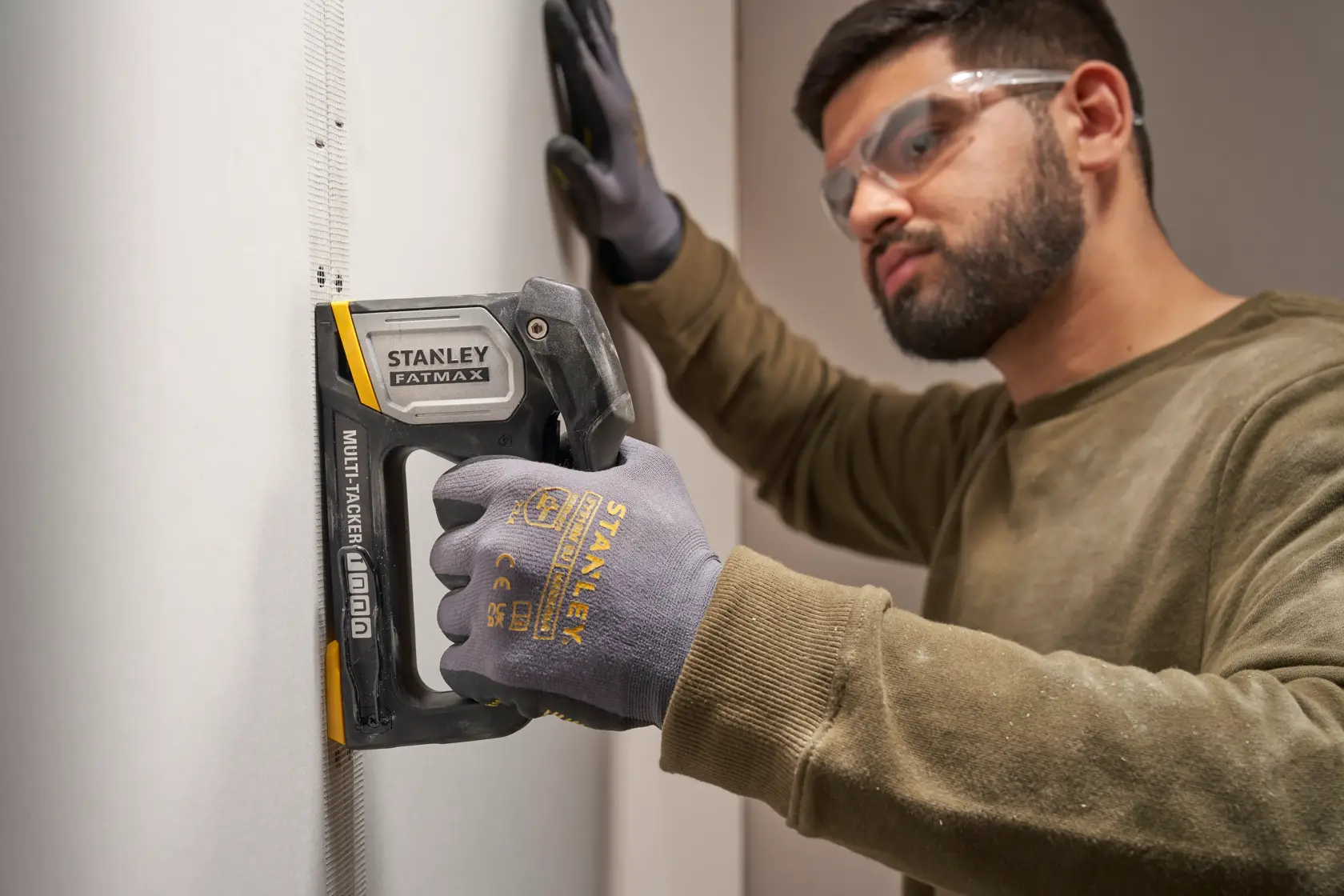 STANLEY FATMAX FMHT70401-0 multitacker used on drywall by person wearing STANLEY gloves, side view.