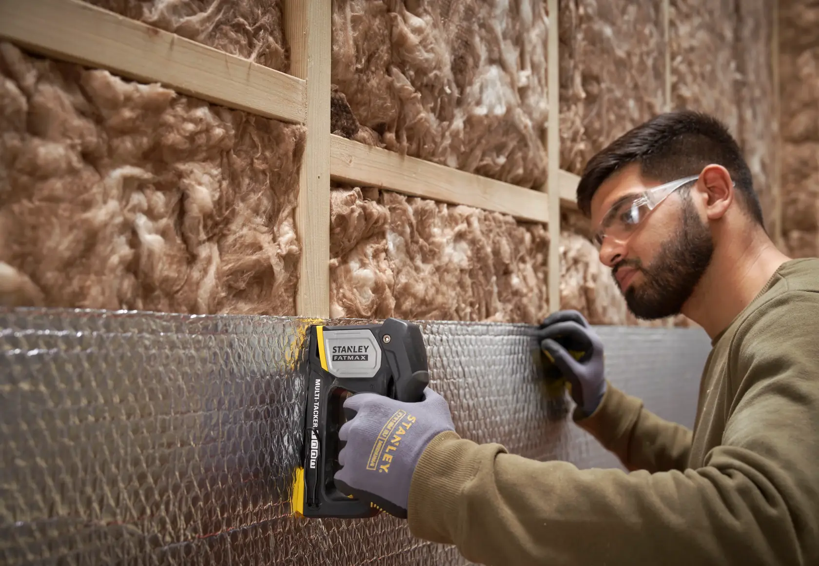 Photo of STANLEY FMHT70401-0 hand stapler being used to secure insulation with gloved hand, construction setting.