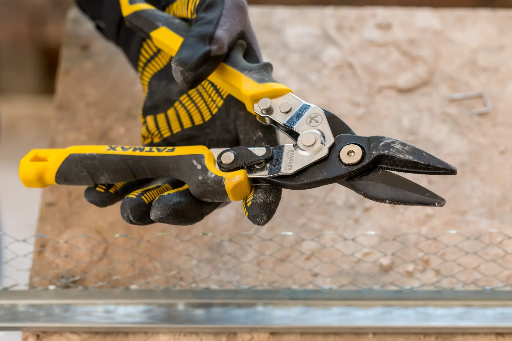 STANLEY FMHT73756-0 aviation snips with yellow and black handles held by gloved hand, cutting wire mesh.