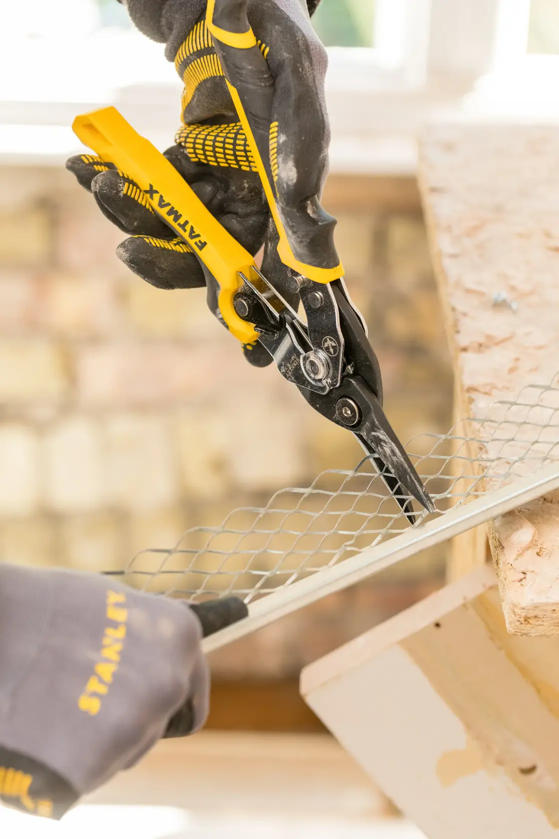 STANLEY FMHT73756-0 aviation snips cutting metal mesh, close-up, with gloved hands in a workshop.