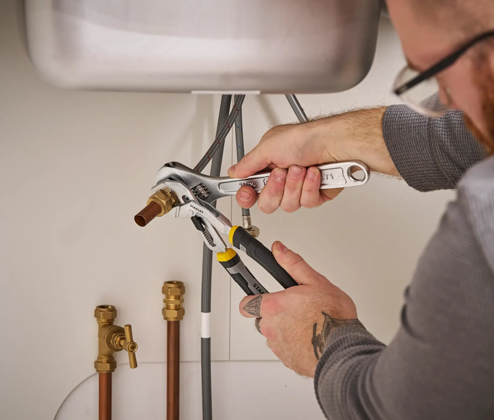 STANLEY FMHT75502-0 pliers used under a sink to grip a pipe fitting during plumbing work.