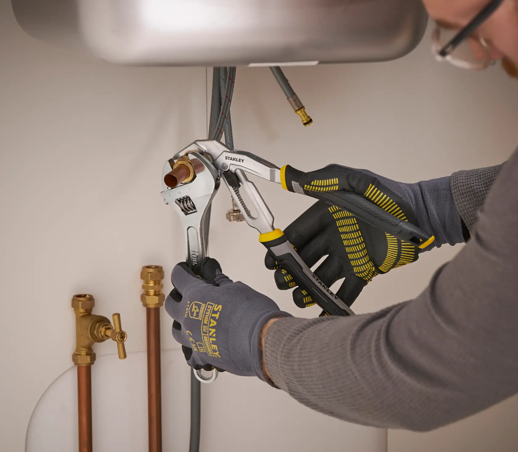 STANLEY FMHT75510-0 adjustable wrench in use under sink with plumbing pipes, close-up photo.