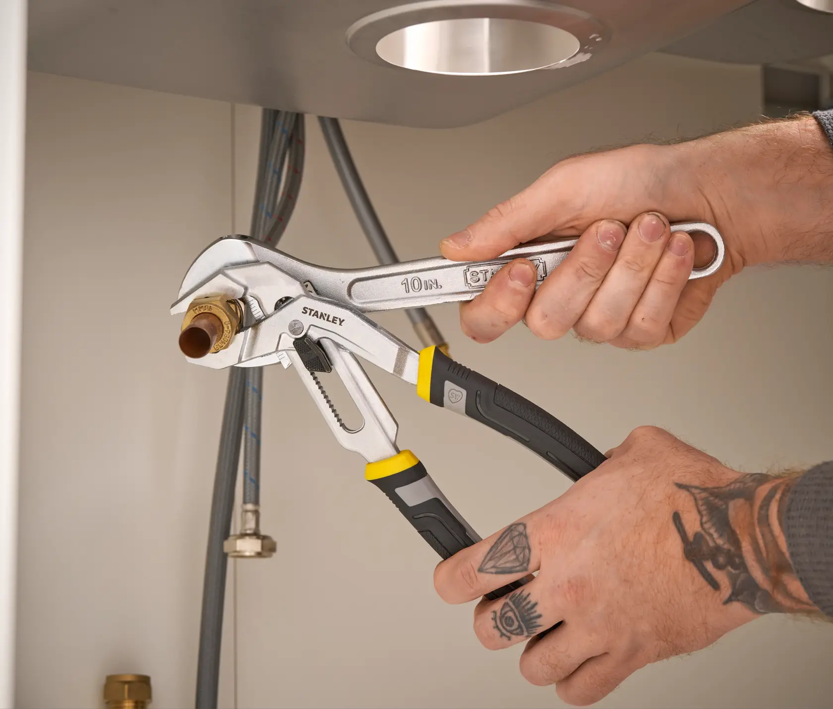 STANLEY FMHT75510-0 adjustable pliers with black and yellow handles used to grip a pipe fitting under a sink.