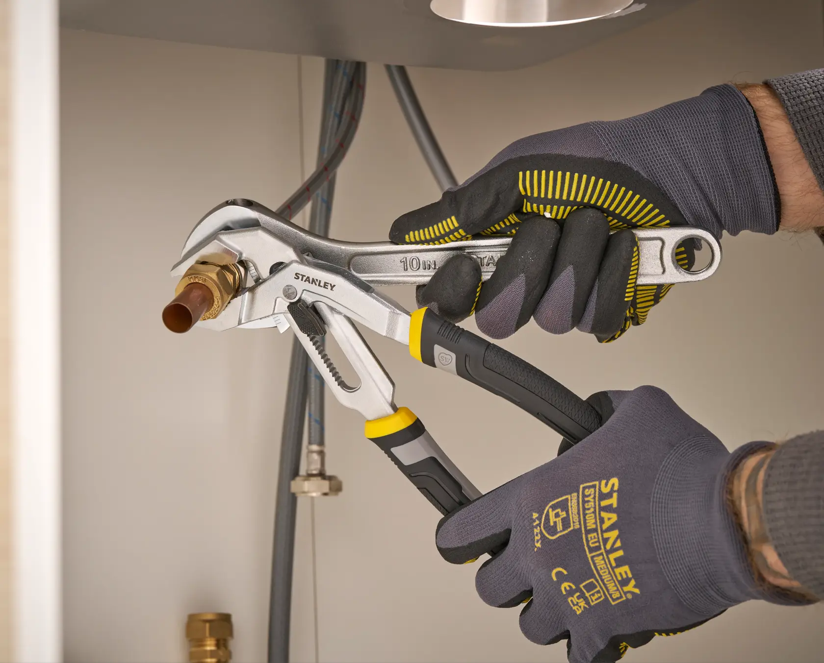 STANLEY FMHT75510-0 adjustable wrench used to tighten a pipe fitting by a gloved hand, close-up action view.