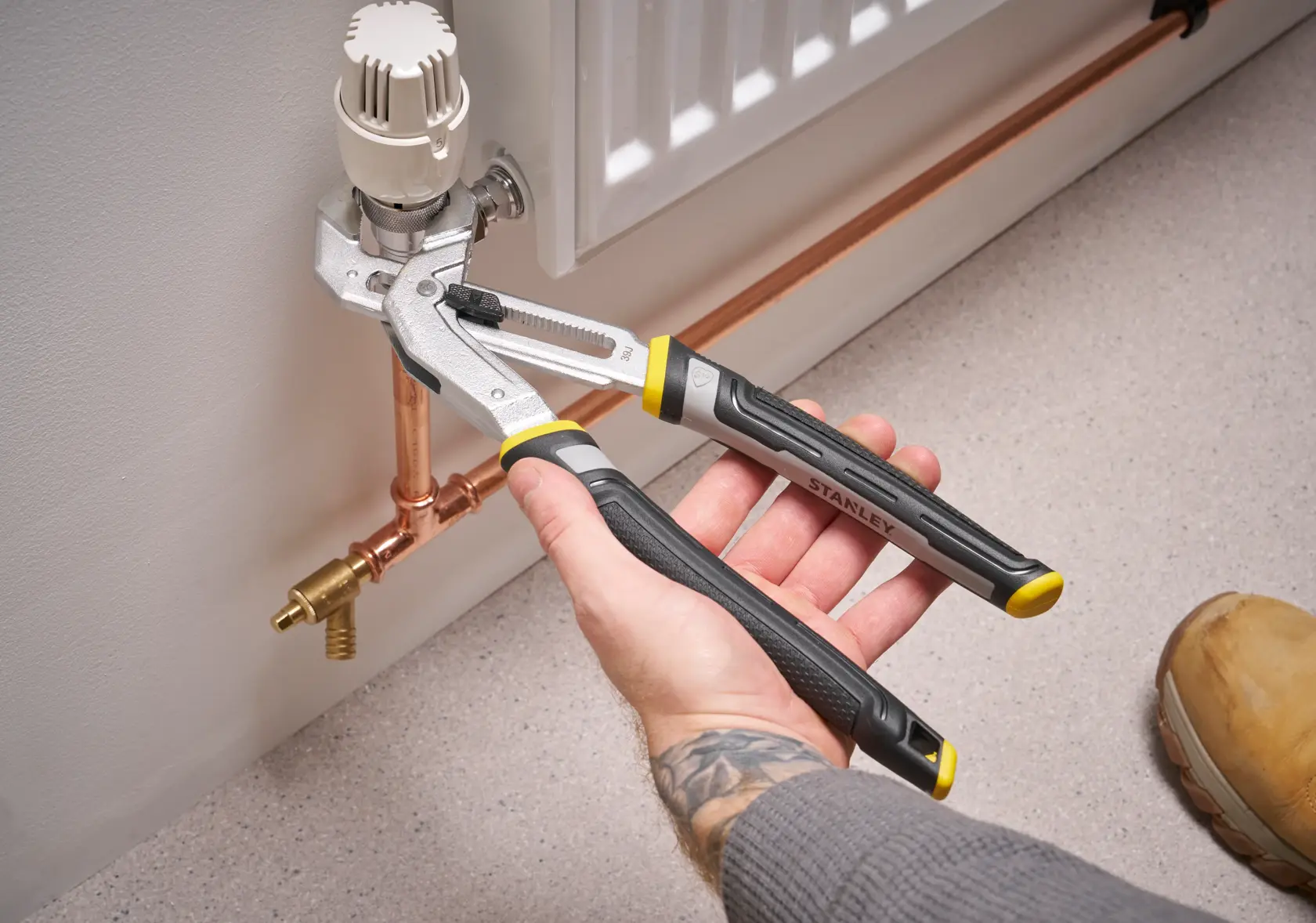 STANLEY FMHT75512-0 adjustable pliers used to tighten a radiator valve, shown in use on copper piping.