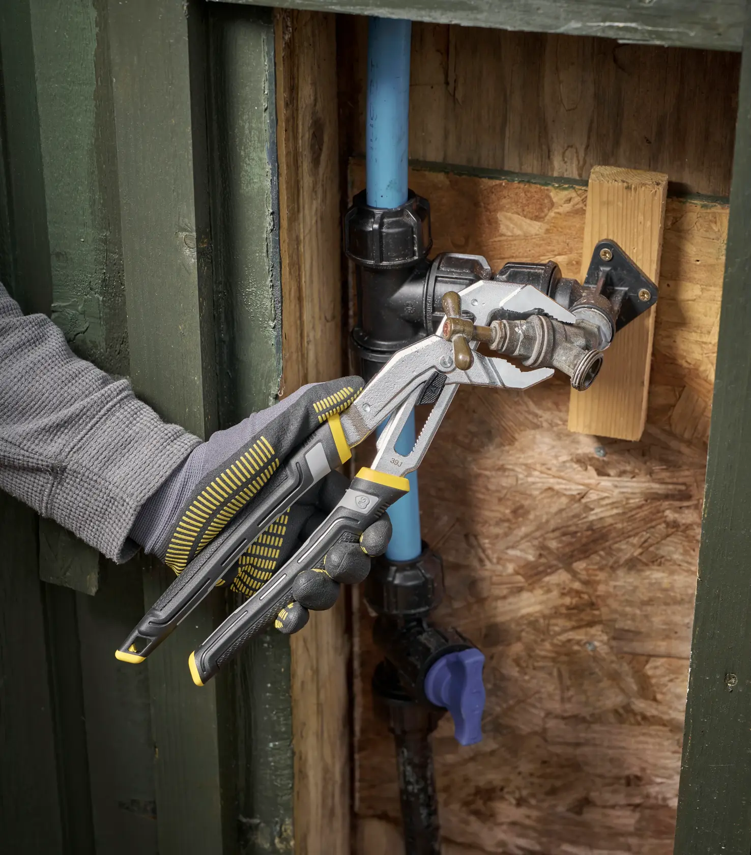 STANLEY FMHT75512-0 water pump pliers in use on an outdoor faucet, close-up view, product held by gloved hand.