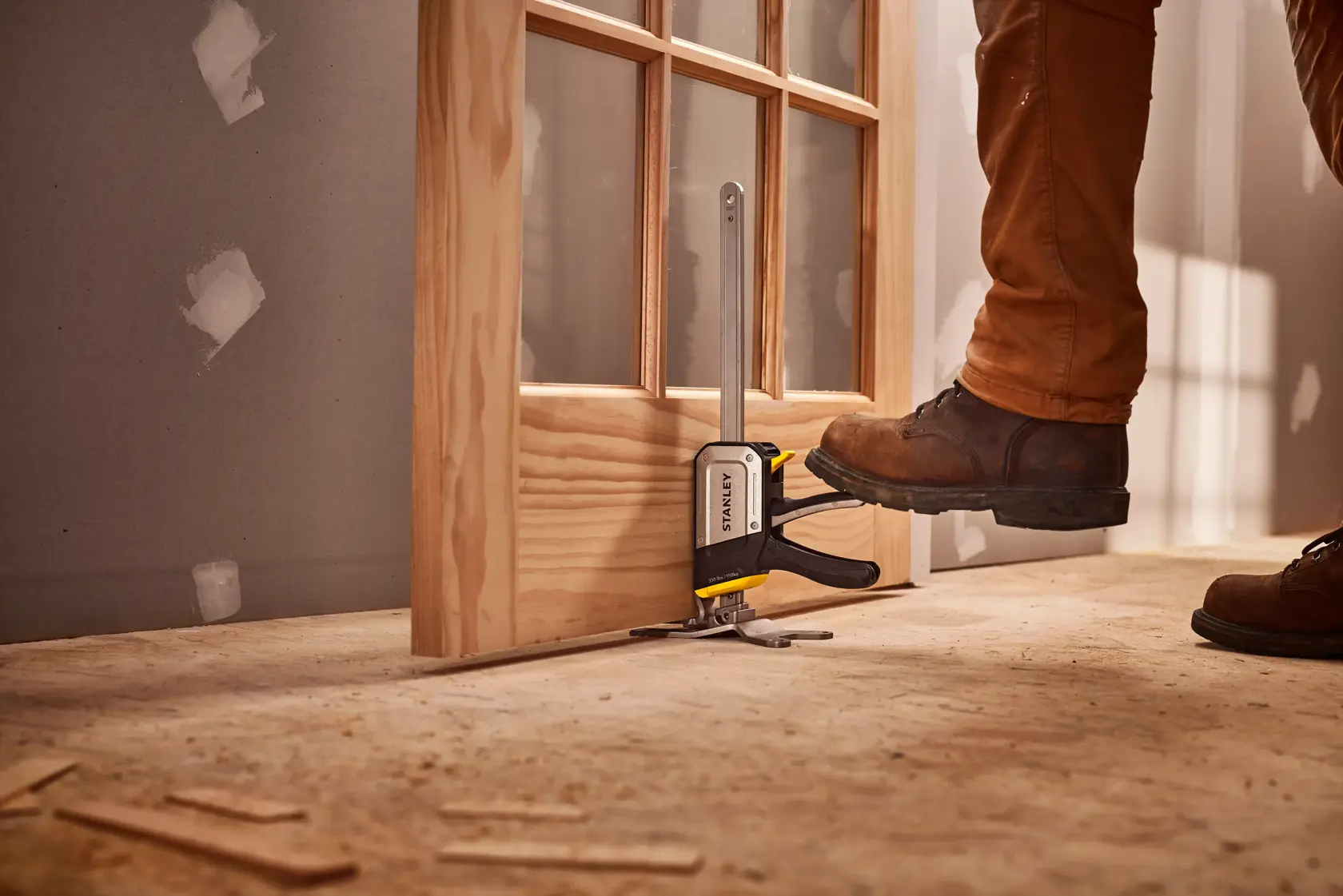 STANLEY FMHT83550-1 Türmontagewerkzeug im Einsatz, Fuß auf Hebel, Holztür, Baustelle.