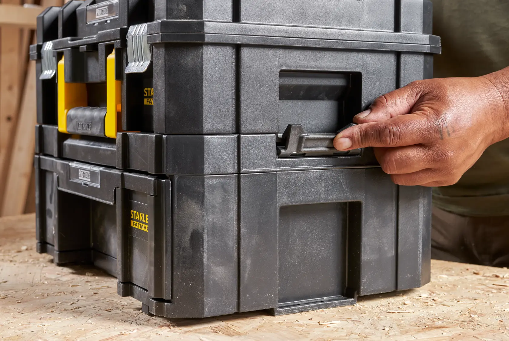 STANLEY FMST1-71968 black stackable toolbox with yellow handles, photography showing latch being opened by hand.