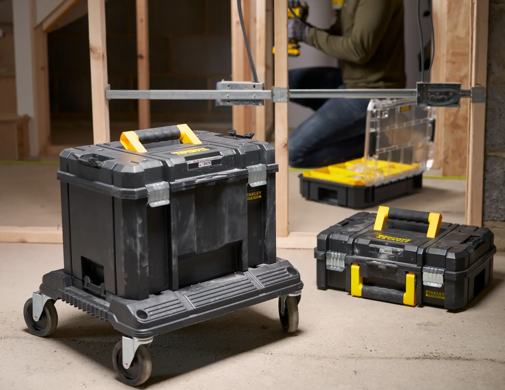 STANLEY FMST1-71971 toolbox on wheeled base, black with yellow handle, in workshop setting.