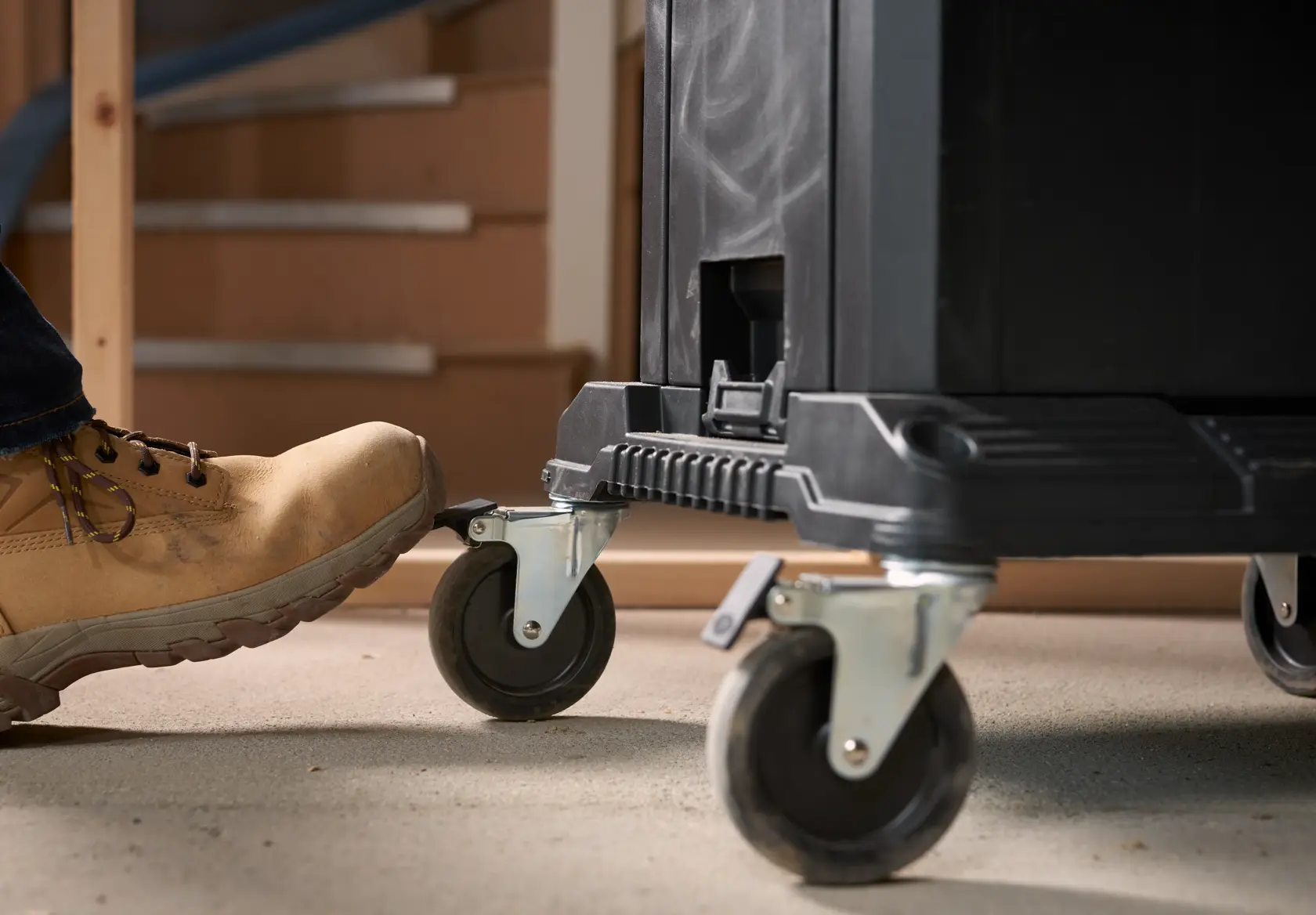 STANLEY FMST1-71972 tool chest caster wheels close-up with foot pressing brake in workshop.