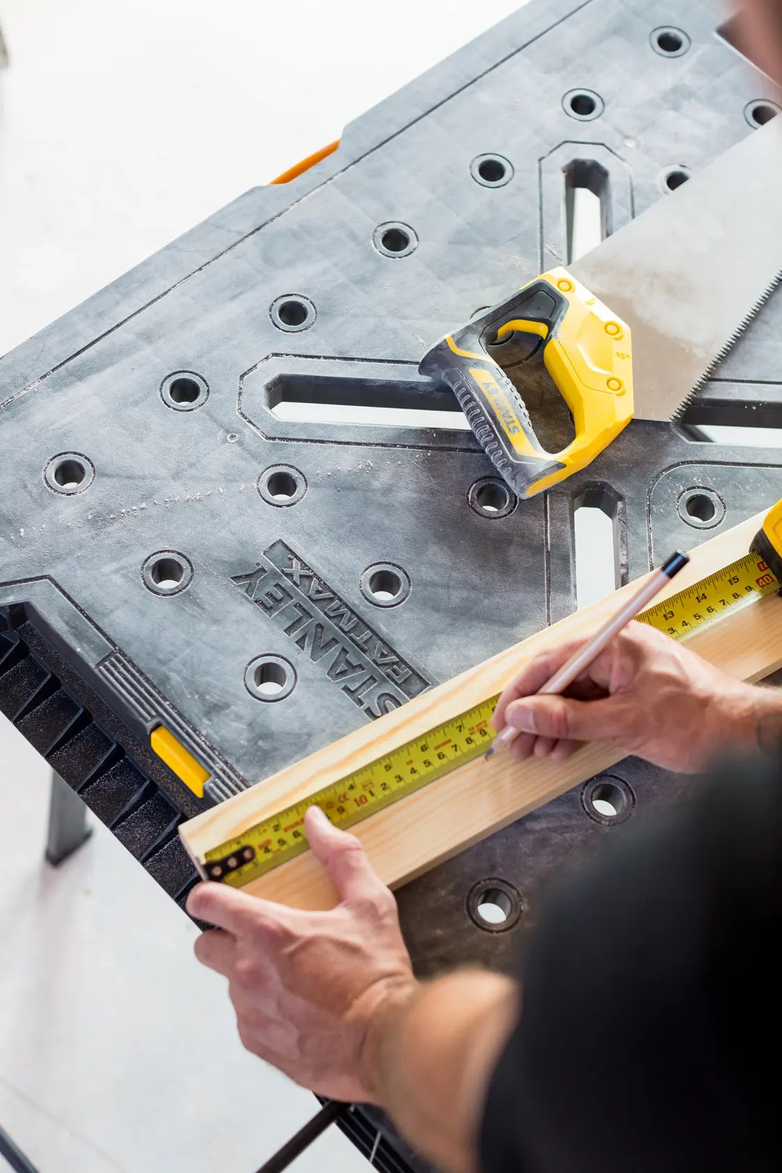 STANLEY FMST1-75672 workbench with hand saw and tape measure, wood being marked for cutting.
