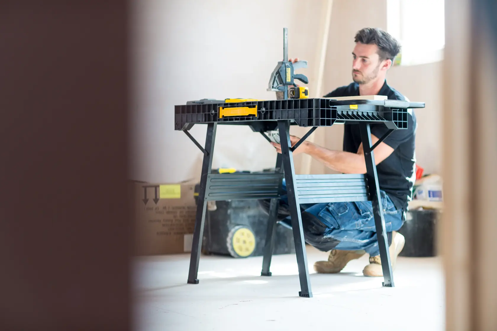 Photo of STANLEY FMST1-75672 workbench in use at construction site, person kneeling beside black folding table.