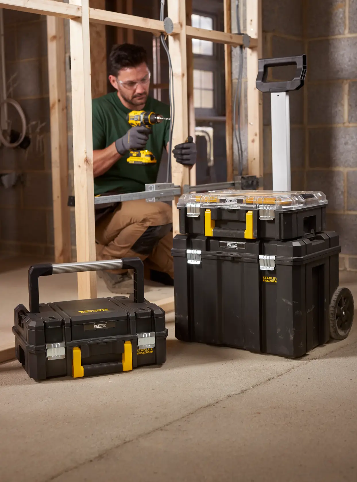 STANLEY FMST1-75753 modular black toolboxes with yellow latches, one on wheels, on a construction site.