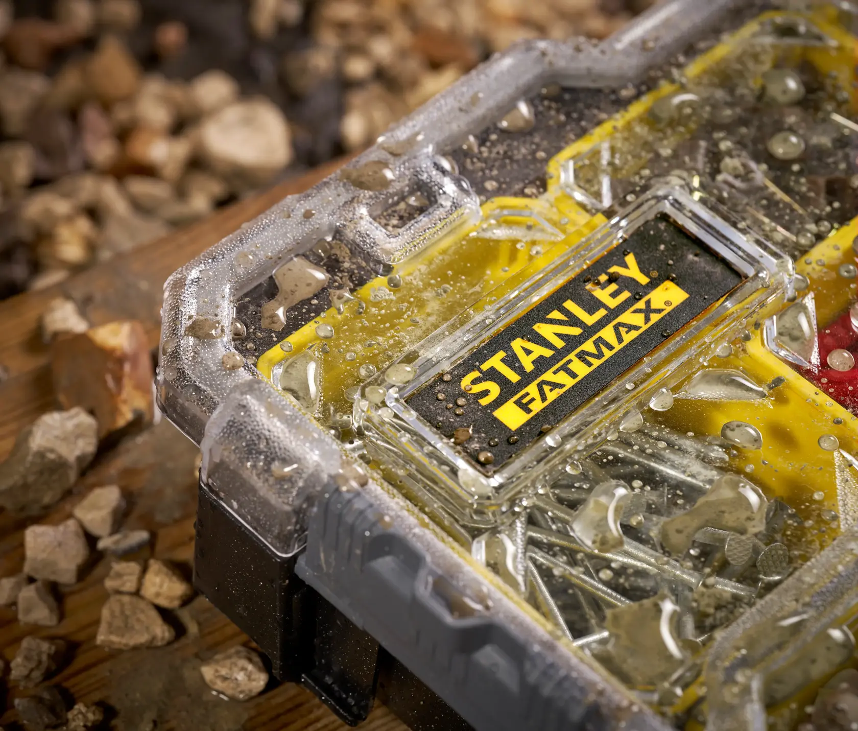 Photo of STANLEY FMST1-75781 waterproof small parts organizer with water droplets on clear lid, surrounded by rocks.