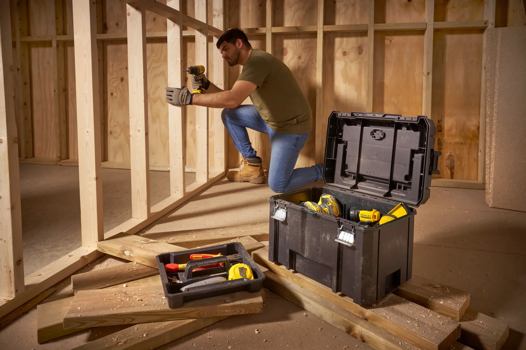 Photo of STANLEY FMST1-75796 tool box with open lid, tools inside, placed on wooden planks at a construction site.