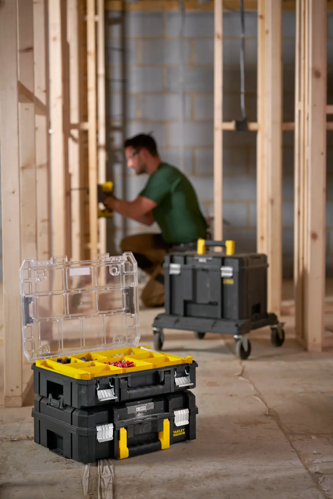 STANLEY FMST82967-1 black and yellow tool organizer box with clear lid open, stacked on another box at construction site.