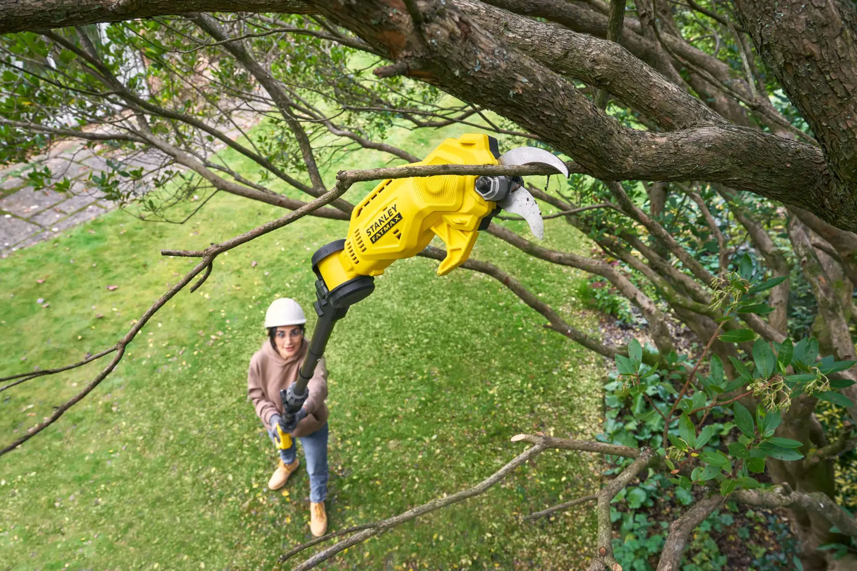 STANLEY SFMCPP632D1 cordless yellow pole pruner cutting a tree branch in outdoor garden.