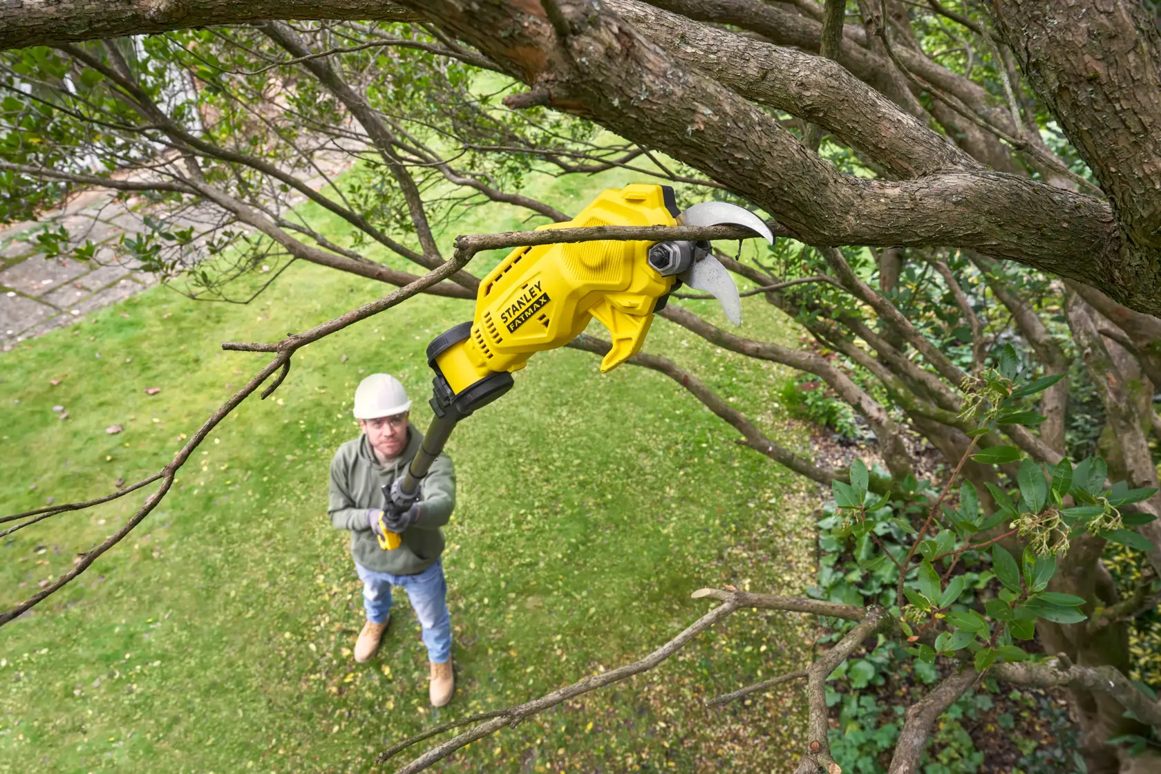 STANLEY SFMCPP632D1 cordless pole pruner trimming tree branches in garden, yellow tool held overhead.