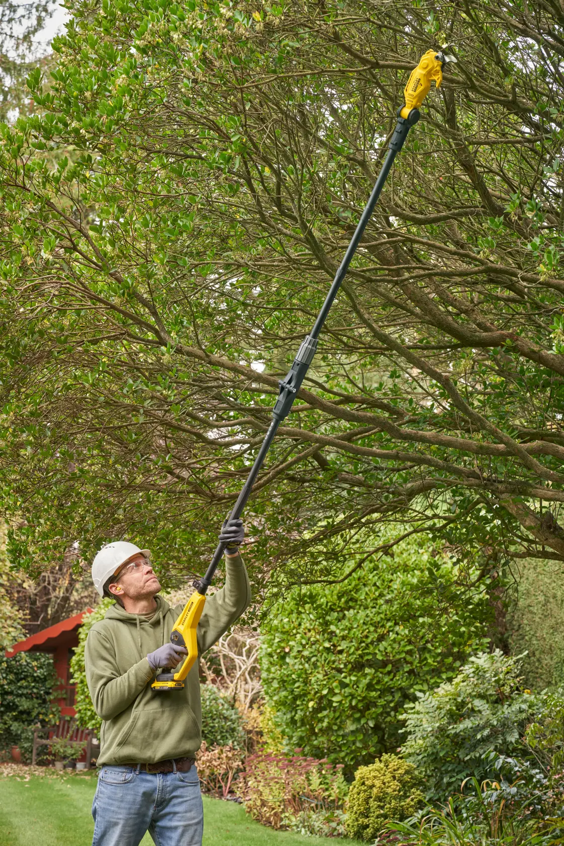 Photo of STANLEY SFMCPP632D1 pole saw being used to trim high tree branches in a garden.