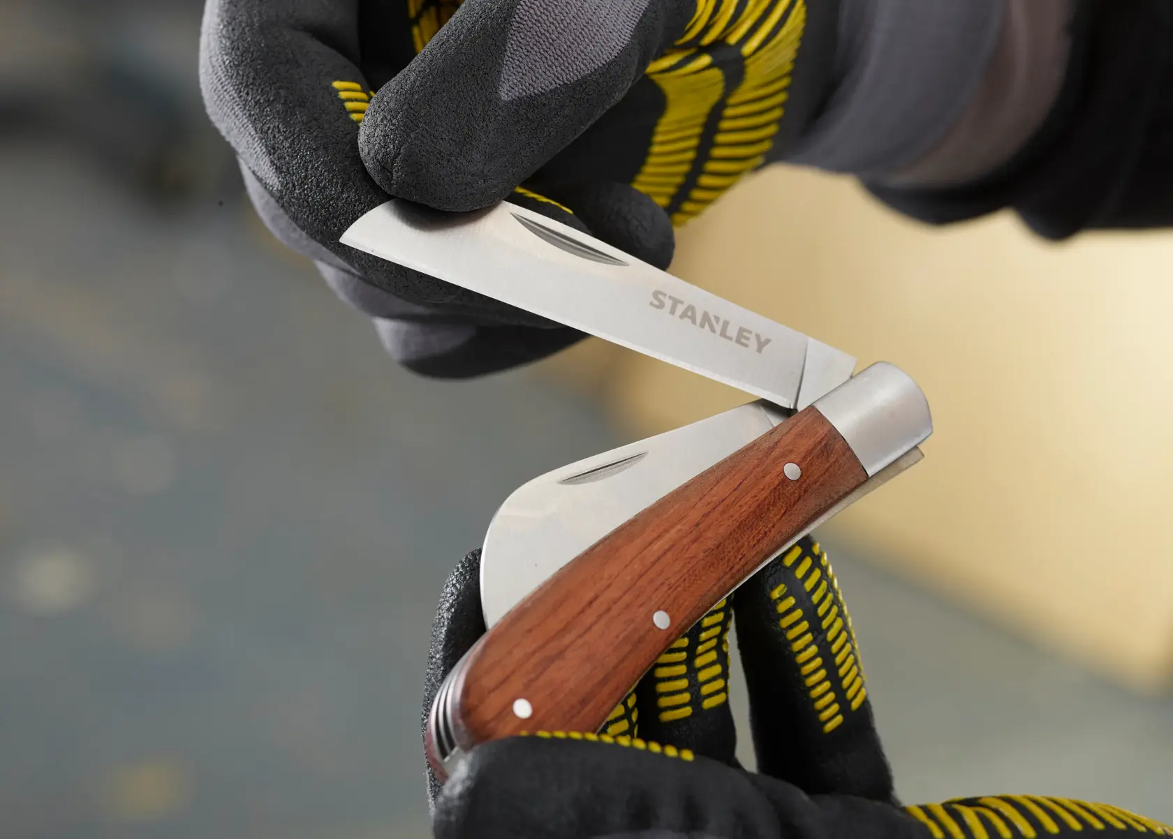 STANLEY STHT0-62687 folding pocket knife with wood handle, close-up held by gloved hands.