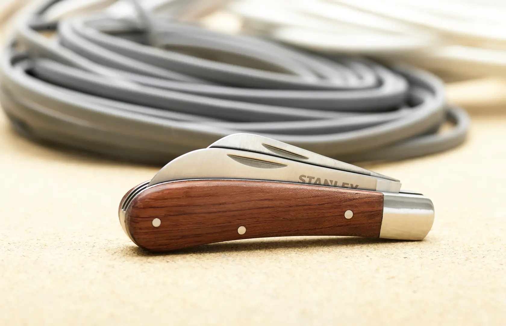 STANLEY STHT0-62687 pocket knife with wood handle and folded blade on beige surface, coiled cables in background.