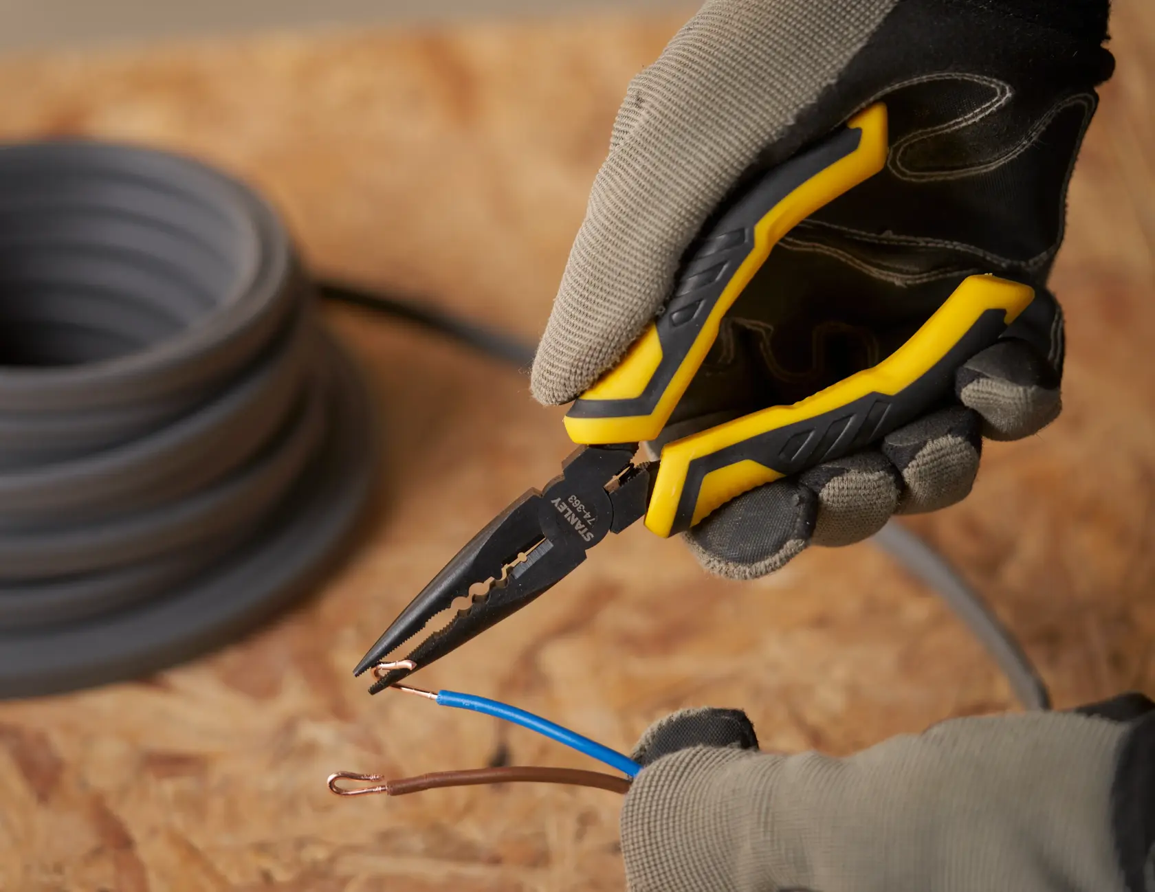 STANLEY STHT0-74363 pliers with yellow and black handle stripping electrical wires, close-up.