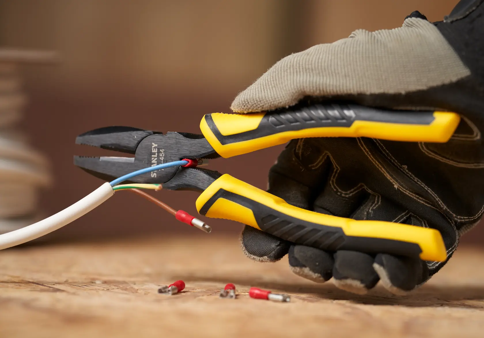 Photo of STANLEY STHT0-74454 combination pliers with yellow and black handle cutting electrical wires, held by gloved hand.
