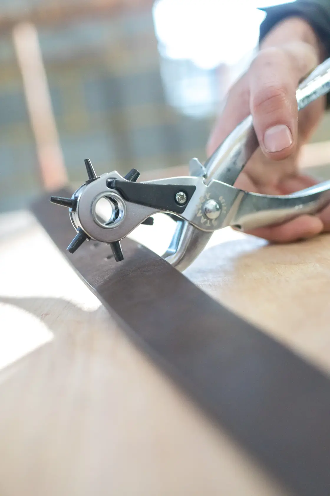 STANLEY STHT0-75044 leather hole punch pliers used on a dark leather strap, closeup action photography.