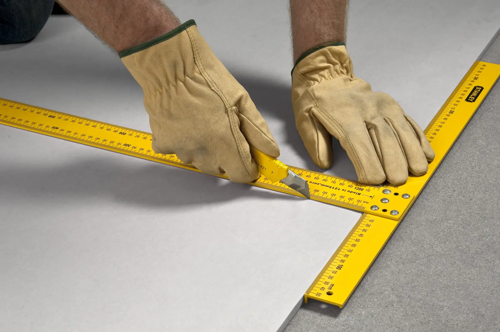 STANLEY STHT1-05894 gelbes Trockenbauquadrat von behandschuhten Händen auf einer ebenen Fläche verwendet.