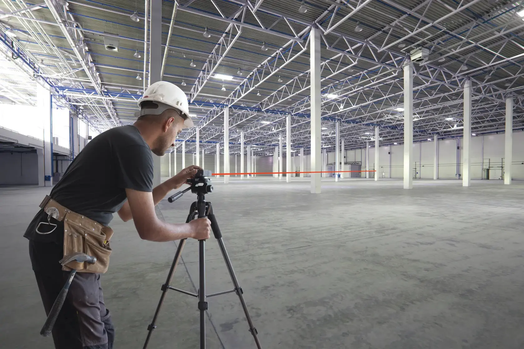 STANLEY STHT1-77140 tripod-mounted laser level used by construction worker in large empty warehouse.