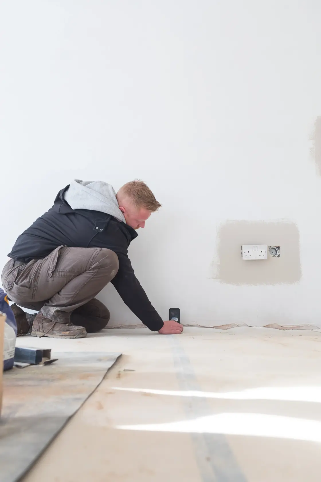 Person using STANLEY STHT1-77142 laser distance measurer on wall in construction setting.