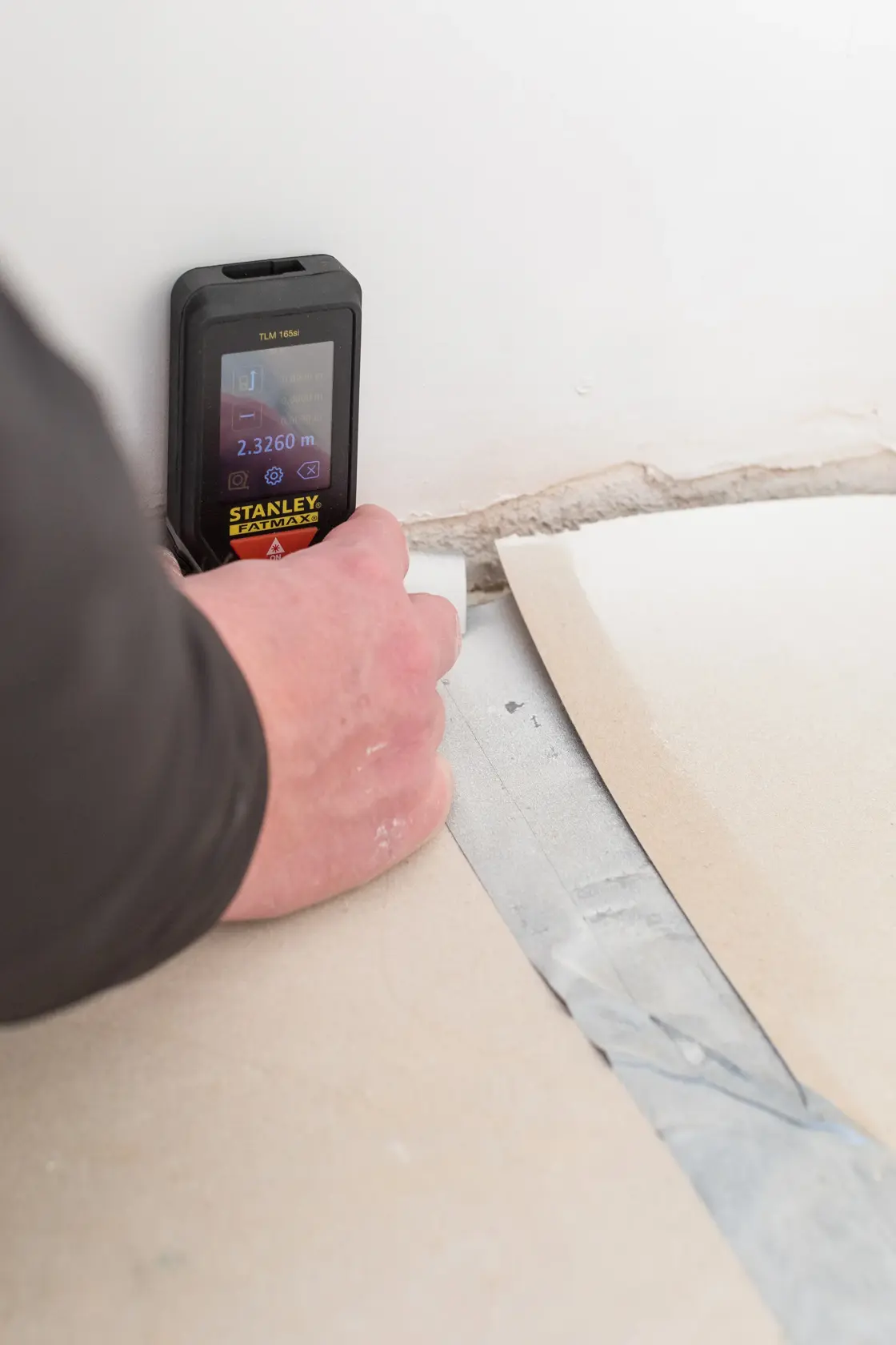 STANLEY STHT1-77142 laser distance measurer being used on a wall and floor corner.