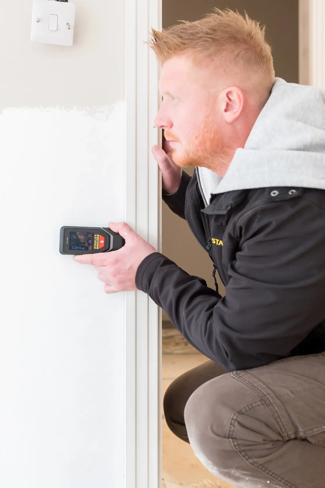 Person using STANLEY STHT1-77142 electronic detector on white interior wall, close-up view.