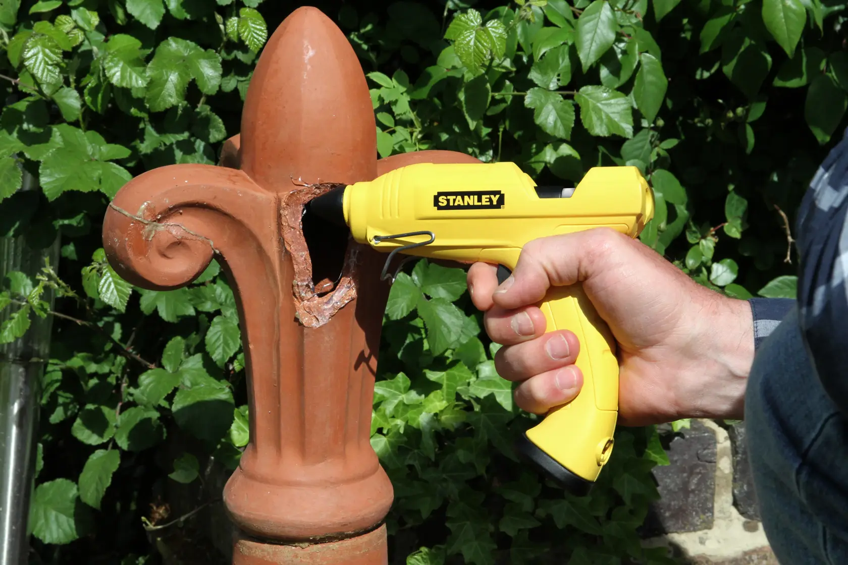 Stanley STHT6-70416 gelbe Klebepistole zur Reparatur eines Terrakotta-Ornaments, von Hand gehalten.