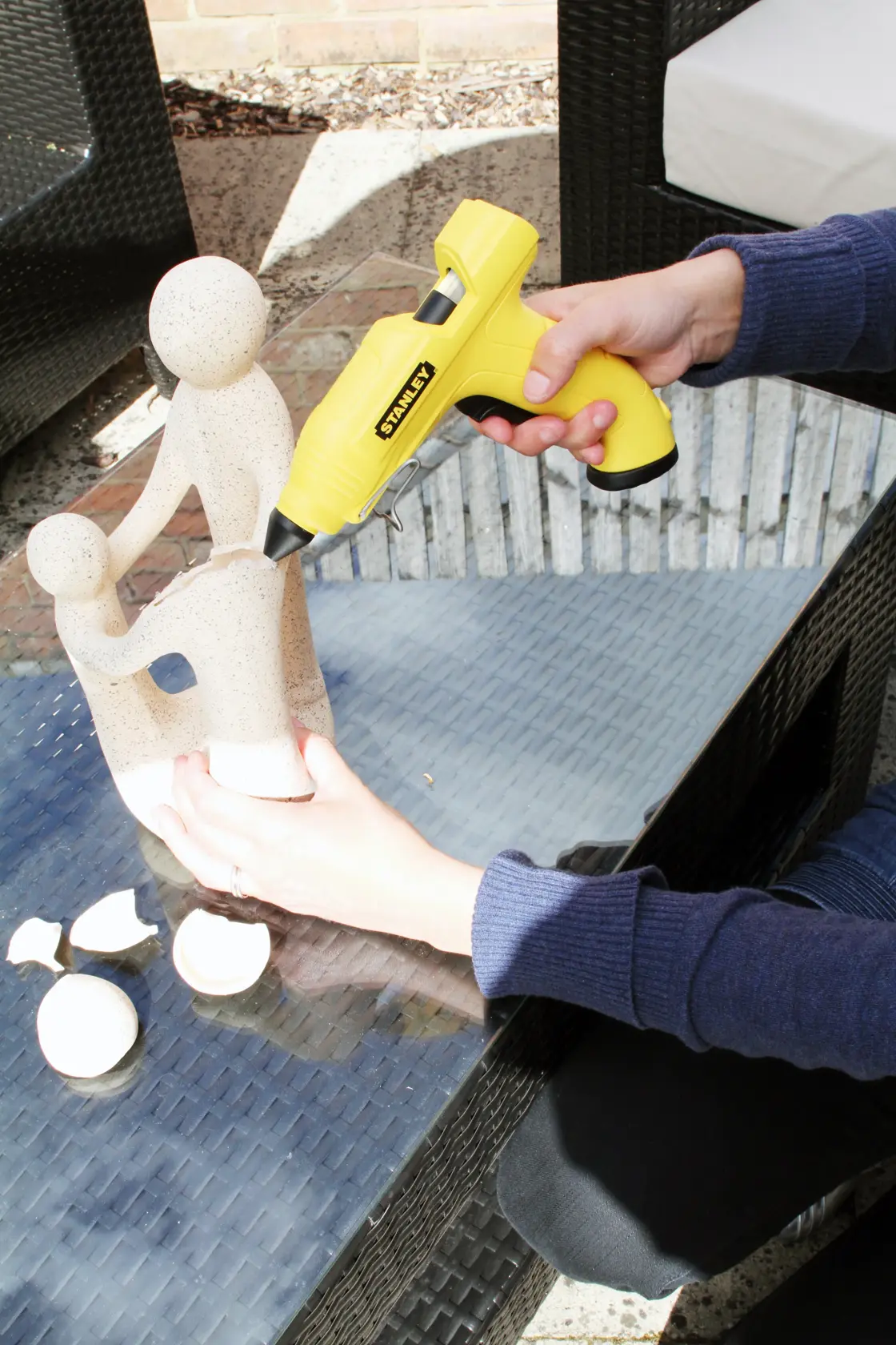STANLEY STHT6-70416 Fotografie einer gelben Heißklebepistole zur Reparatur einer Steinskulptur auf Glastisch.