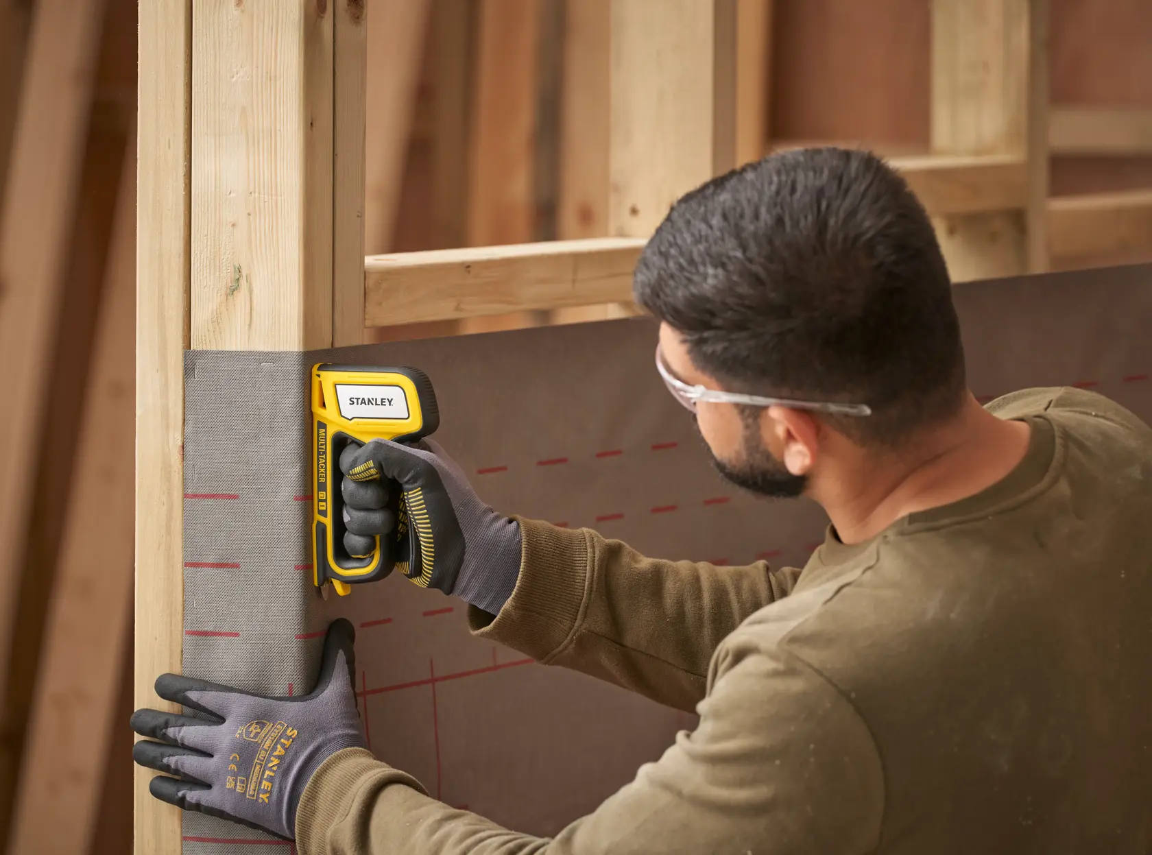 Foto des STANLEY STHT70440-0 Tackers an einem Wandrahmen, Arbeiter trägt Handschuhe.