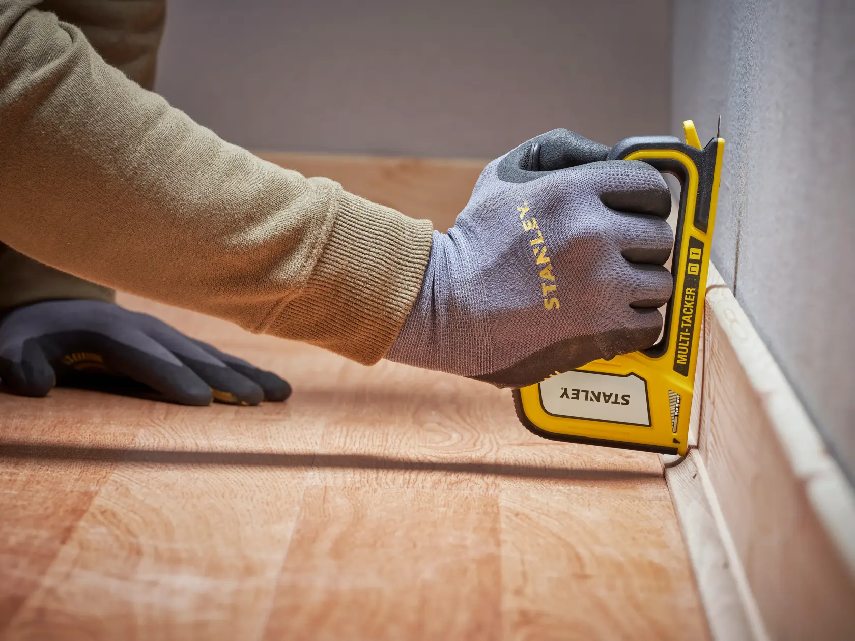 Stanley STHT70440-0 manueller Tacker, gelb und schwarz, von einer behandschuhter Hand an der Fußleiste verwendet.