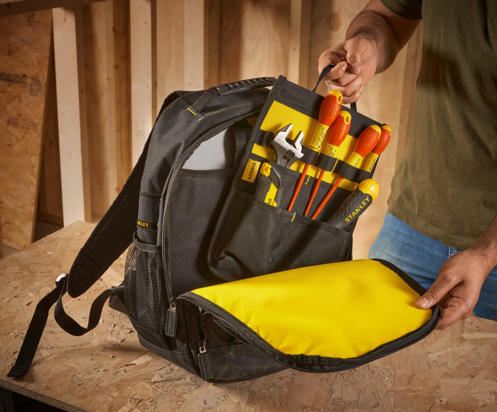 STANLEY STST1-72335 Werkzeug-Rucksack mit gelbem Innenraum, gefüllt mit Handwerkzeugen, offen gezeigt auf Tisch.