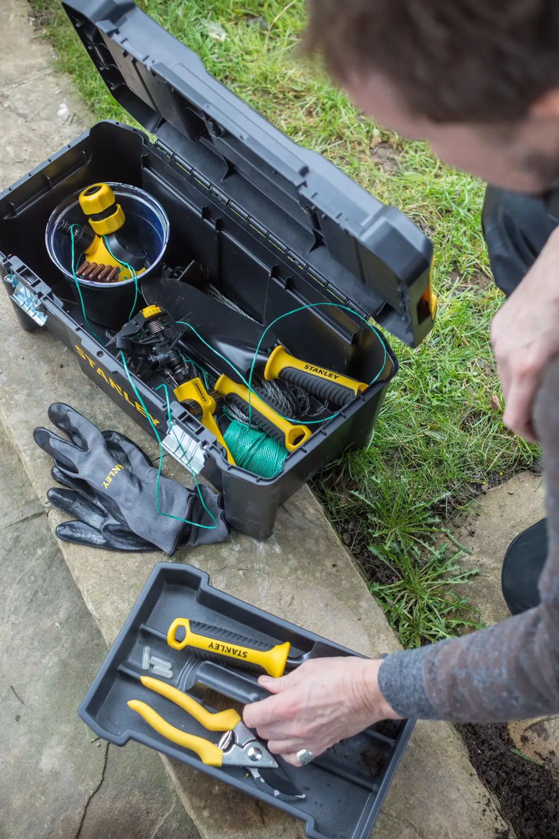 STANLEY STST1-75521 Werkzeugkasten mit offenem Deckel, Gartenwerkzeuge und Handschuhe sichtbar, Außenansicht von oben.